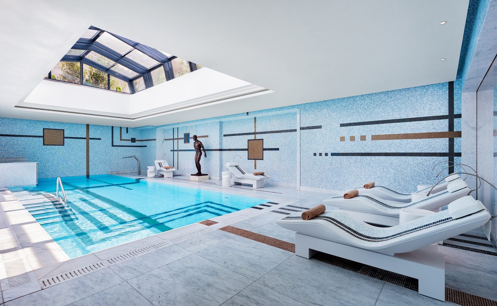 Indoor pool lined in pale blue SICIS glass mosaic under a skylight, with white loungers on the deck